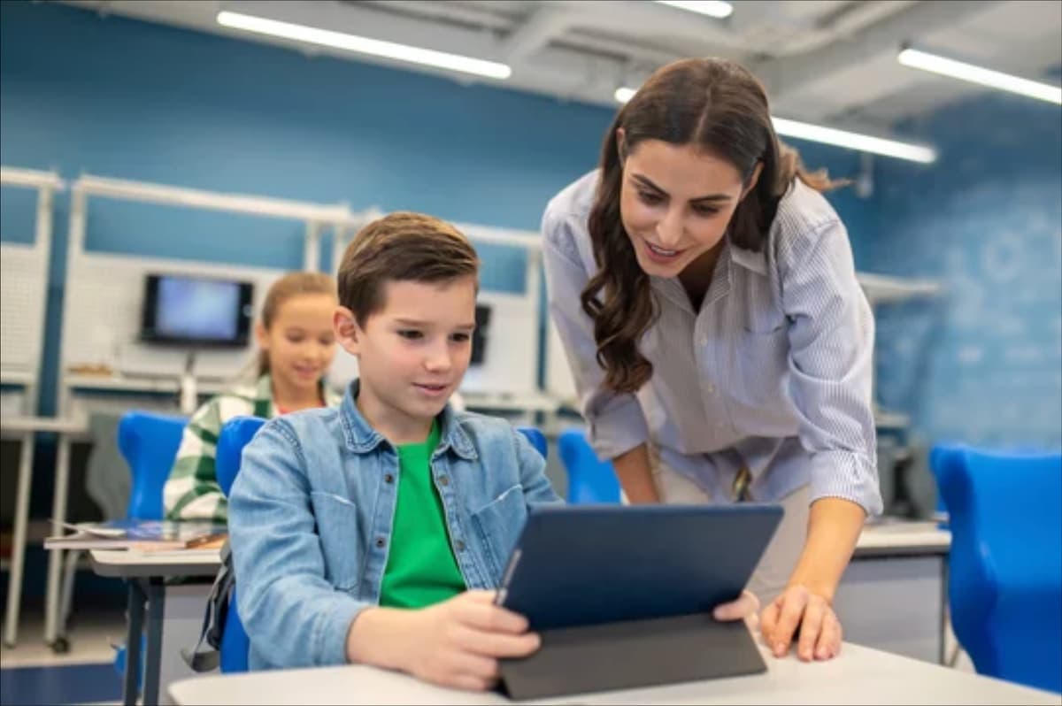 A student working on a tablet while a teacher looks on