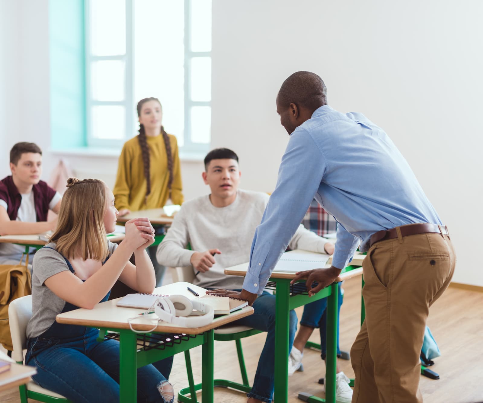 A teacher in conversation with a class of students at their desks