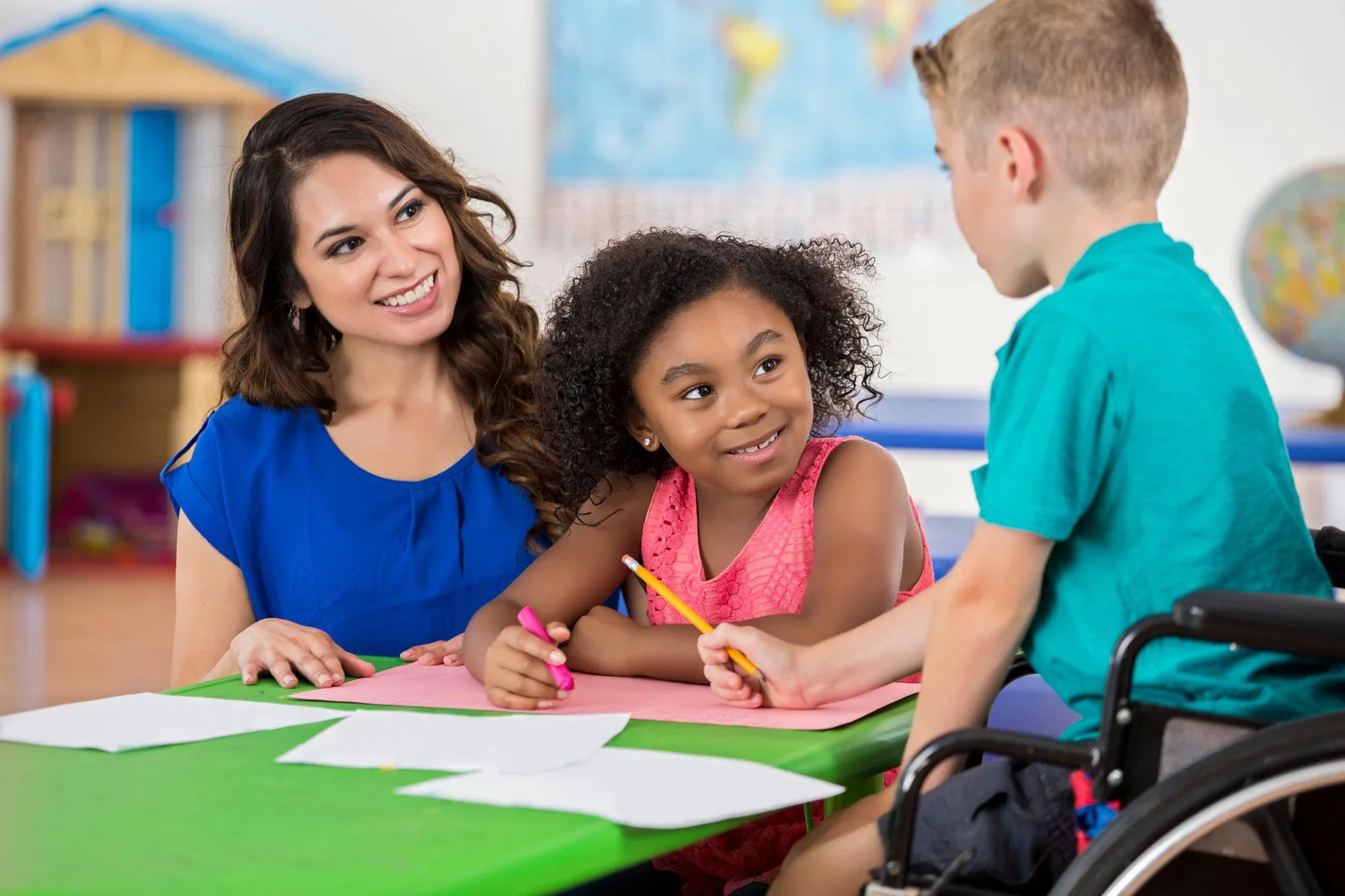 A teacher crouched at a pupil's desk, talking with him one to one while the class works